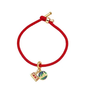 Red braided cord bracelet with gold charms and travel themed city landscape enamel pendant