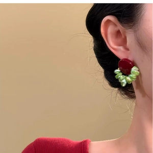 Close-up of geometric acrylic shell earrings in burgundy and green worn by a model