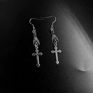 Macro detail of gothic earrings featuring a bat and cross design in vintage silver finish