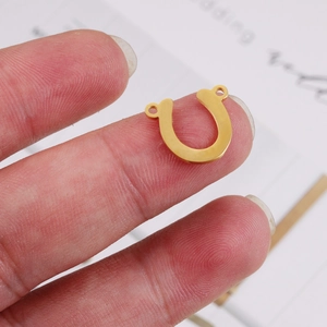 Close-up of a small golden U-shaped stainless steel connector held by fingers for DIY jewelry