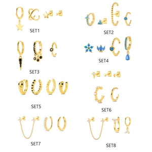 Eight sets of gold earrings including studs, hoops, and ear cuffs with blue or black gems