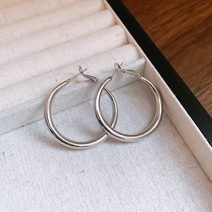 Close-up of polished silver C-shaped hoop earrings inside a cream jewelry box