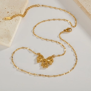 Elegant gold-plated stainless steel necklace with a 3D bow pendant on a textured stone base