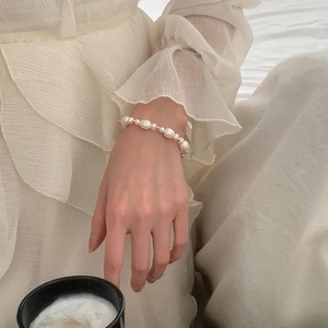 Elegant baroque pearl bracelet on wrist with gold spacers and white chiffon background