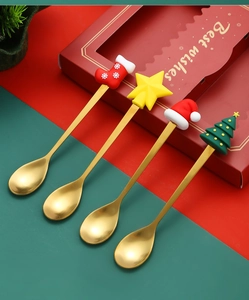 Detail of four golden Christmas spoons with silicone festive charms in a red gift box