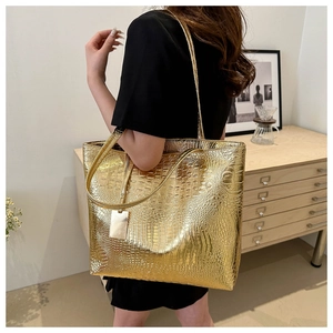 Detail shot of golden tote bag featuring embossed crocodile pattern and long strap