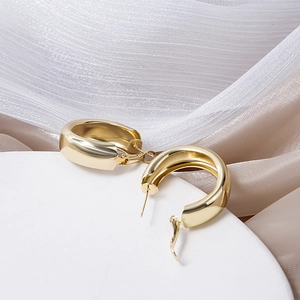 Detailed view of polished wide gold hoop earrings on a silk background tray