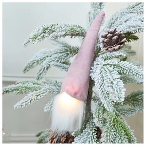 Close-up of a pink glowing Christmas gnome with warm LED light on a snowy pine branch