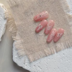 Detailed view of pink press-on nails with white floral patterns and silver rhinestones