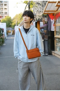Detail of a bright orange nylon crossbody bag with adjustable strap worn by male model
