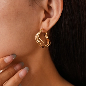 Close-up of golden irregular wave geometric earrings showing flowing metallic texture