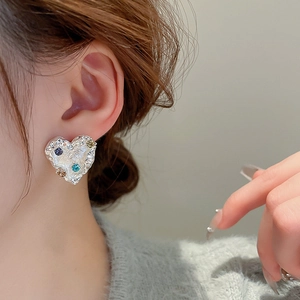 Close-up of heart earrings with multi-colored stones on textured silver metal finish