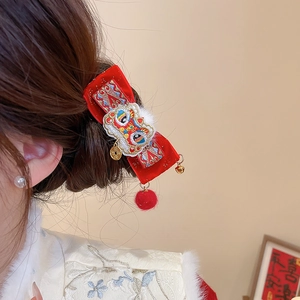Detail view of red velvet bow hair clip with embroidered lion and golden bells