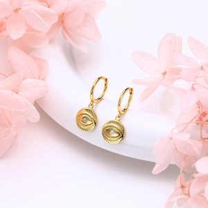 Detail of gold Evil Eye earrings with white crystal stone hanging by pink flowers