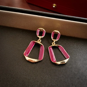Macro detail of geometric gold earrings with magenta enamel on a dark leather display