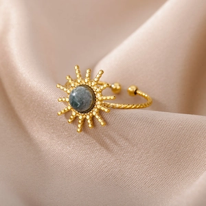 Macro shot of gold sunbeam ring with dark stone inlay on silk fabric backdrop