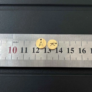 Macro shot of 10mm golden stainless steel round letter charms A and K on a ruler