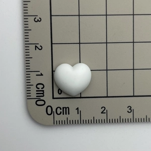 Size demonstration of white heart resin charm with Sweet text using a metric scale ruler