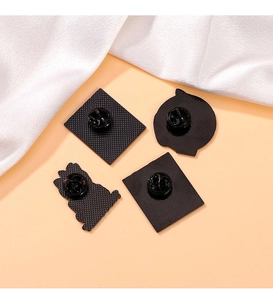 Detail view of four black metal brooch backs with secure rubber clutches on peach background