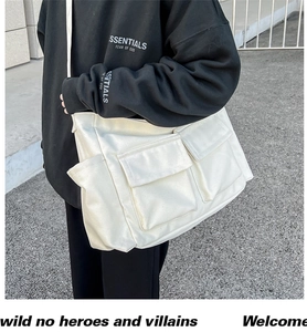 Detail of a large cream canvas messenger bag with double front pockets and wide strap