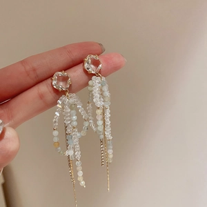 Detail of long tassel earrings with clear faceted crystals and gold chains held in hand