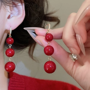 Detail of red resin triple bead drop earrings with gold plated diamond-set ear hooks