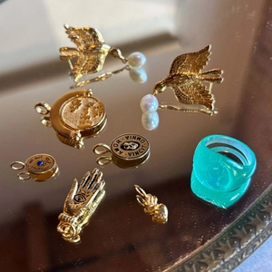 Flat lay of gold coin and heart charms with a green ring on a vintage mirror