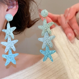 Detail of woven raffia star earrings featuring light blue and mint green fringe pendants