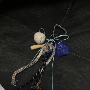 Mini baseball keychain with bat, blue leather glove, and woven rope on dark fabric