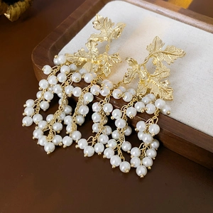 Dettaglio degli orecchini a foglia d'acero dorata con eleganti nappe di perle bianche