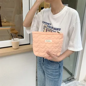 Detailed close-up of a peach quilted makeup bag with heart patterns held by a woman