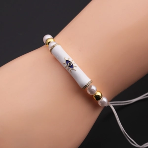 Detail of evil eye bracelet with white pearl, gold beads, and ceramic tube on hand