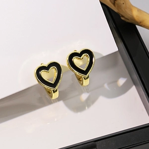 Détail de boucles d'oreilles cœur dorées avec émail noir sur un fond en bois minimaliste