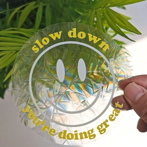 Hand holding a round holographic suncatcher sticker with slow down smiley face text
