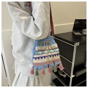Detail view of the colorful ethnic embroidery and tassels on the blue bucket bag