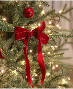 Detail of a red velvet Christmas bow ornament hanging on a festive decorated pine tree branch