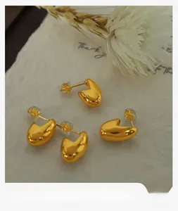 Close-up of minimalist gold-plated bean stud earrings on rustic textured paper with dried flower