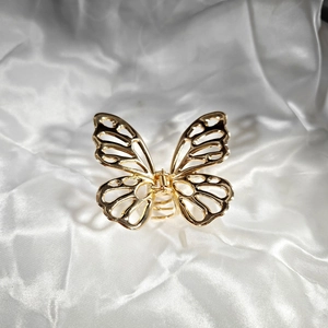 Detail of a golden metal butterfly hair claw clip with intricate hollow design on silk