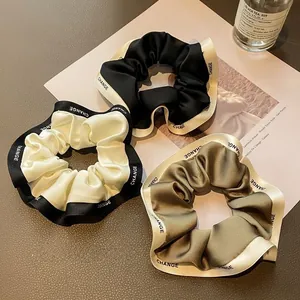 Detailed close-up of three satin scrunchies with CHANGE ribbon trim and silk texture