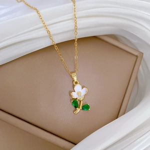 Close-up of gold flower necklace with white petals and green leaf on silk background