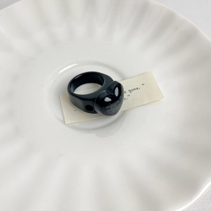 Close-up of a polished black resin heart ring on a white wavy ceramic jewelry tray