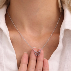Silver butterfly necklace with blue and purple zircons worn by a model on white shirt