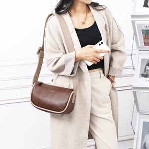 Model met een chocoladebruine lederen crossbodytas met een beige riem in een chique setting