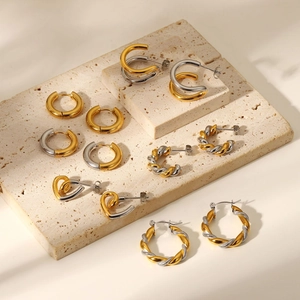 Detailed view of gold and silver mixed-metal hoop earrings on a stone texture base