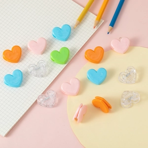 Macro shot of colorful heart-shaped plastic clips on white grid paper with pencils
