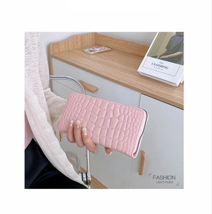 Damen Portemonnaie in Rosa mit Krokoprägung, das von einem Model am Holztisch gehalten wird