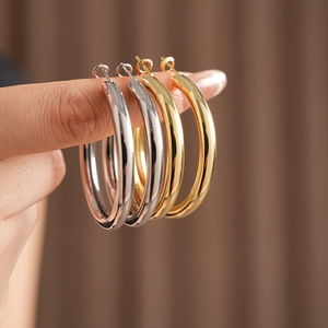 Close-up of gold and silver minimalist metal hoop earrings held by a finger