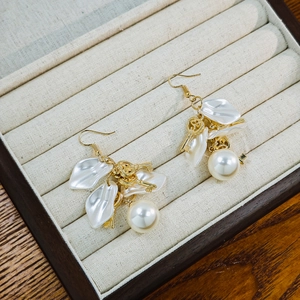 Detail view of pearl earrings with white flower petals and golden key charm in a jewelry box