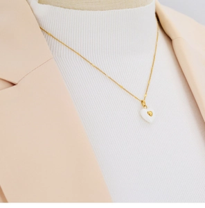 Close-up of a gold heart pendant necklace with white enamel inlay on a female model