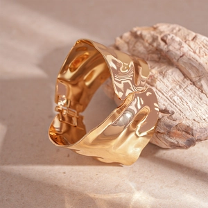 Detailed shot of golden irregular wave wide bangle resting on natural light brown stone